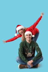 Obraz premium Young couple in Santa hats and Christmas sweaters on blue background