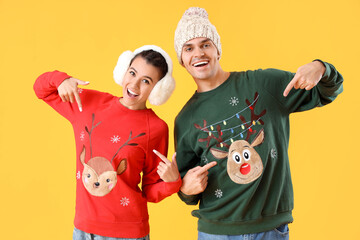 Young couple pointing at Christmas sweaters on yellow background