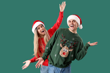 Young couple in Santa hats and Christmas sweaters on green background