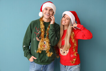 Young couple in Santa hats with tinsel talking by mobile phone on blue background