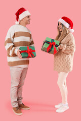 Happy young couple in Santa hats with Christmas presents on pink background