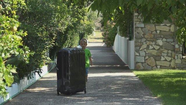 Funny little boy pushing big and heavy suitcase on alley