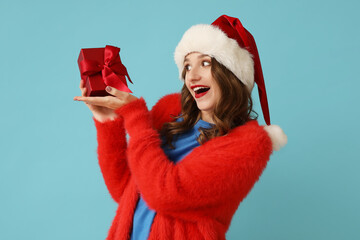 Young woman in Santa hat with Christmas gift box on blue background