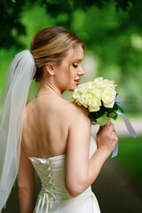 Beautiful and delicate bride in veil and with a bouquet of white roses. 