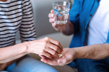 Cropped view of male give medication pill and glass of water his wife