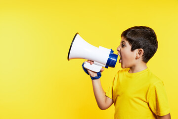 Young boy yells into a megaphone, wearing a glove, with a vibrant yellow backdrop, showing expression.