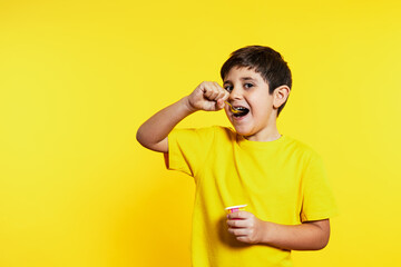Cheerful boy enjoys yogurt, savoring his spoonful against a vivid yellow backdrop, embodying joy...