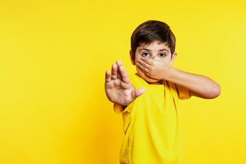 Boy in yellow tee pinches nose and extends hand for stop sign, showing distaste against a yellow...