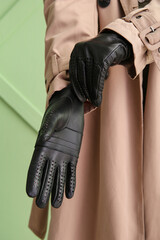 Woman in stylish trench coat wearing black leather gloves against color wall, closeup