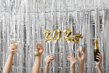 Female hands with champagne bottle, glass and figure 2024 made of balloons on silver tinsel...