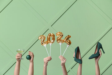 Female hands with high heel shoes, glass of champagne and figure 2024 made of balloons on green...