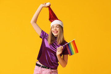Young woman in Santa hat with LGBT flag on yellow background