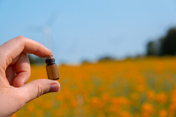 Hand holding test tube with liquid on background of canola flowers field blooming farm. Rapeseed...