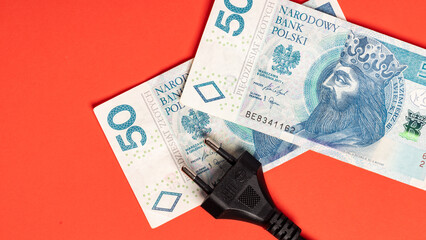 money Polish zloty banknotes and black electric cable with plug lying on red background (selective focus)