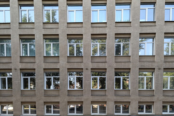 There are many windows in a row on the facade of a city building. a concrete building with many...