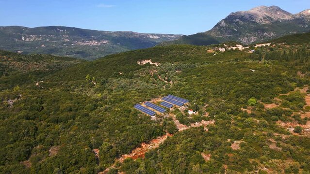 Aerial shot of a drone flying over an array of photovoltaic (PV) panels generating electricity on a remote mountain terrain. Solar panels and renewable energy concept. Sunny summer day.