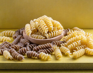 Raw whole grain fusilli pasta and gnocci pasta. Uncooked pasta on yellow background.