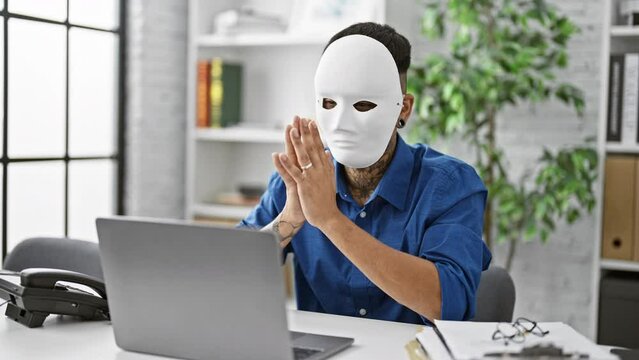 Young latin man hacking, a masked hacker tapping away on his laptop, eyes glued to the screen, poised in his office, ready to commit his next cyber crime