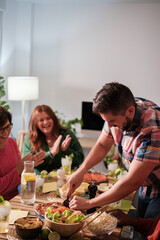 Young man cutting food to offer to his colleagues at a friends dinner. Concept: together, celebration