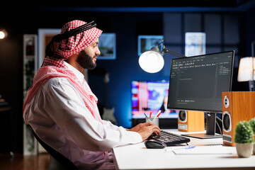 Image shows an Arab software developer working at the pc monitor, seated at a workstation...