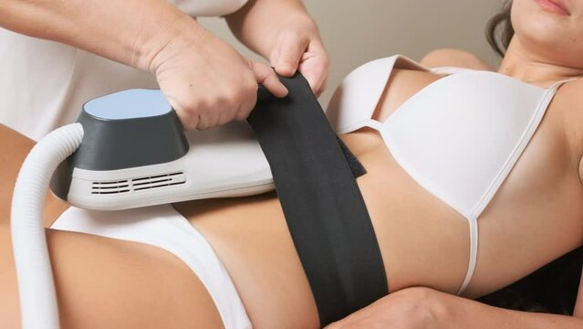 Woman worker of spa salon in work uniform does body sculpting in client abdomen area. Physical care and procedure in light premise concept