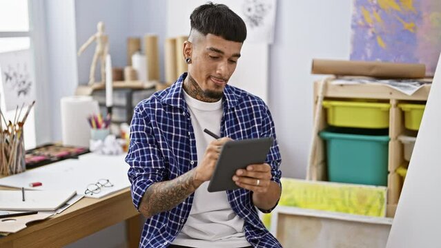 Tattooed young latin man happily drawing on touchpad, brushing up creativity digitally at art studio
