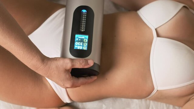 Spa worker massages woman client belly with cellulite remover. Appliance for smoothing skin relief and eliminating flabbiness in adulthood