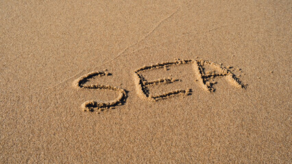 Text SEA handwritten in sand surface. Blue ocean wave washing away message at the beach. Summer holidays beach writing vacation concept