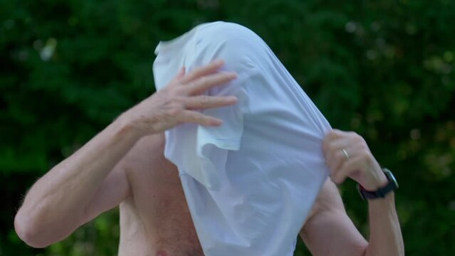 Funny scene of senior man unable to put t-shirt, candid authentic elderly person clothing himself, comedic mix-up