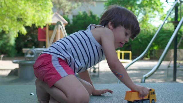 Little Boy Lost in Play with Toy Truck in Summer Park, outdoor imagination during sunny day