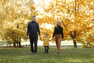 Family day. Happy young mom and dad hold their little child daughter hands walk, have fun outdoor...