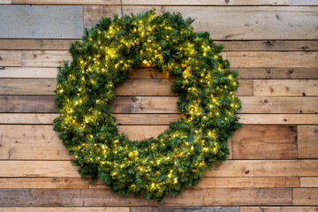 Artificial fir Christmas wreath with gold lights on a rustic wood background

