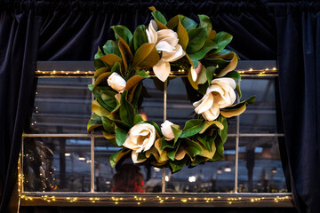 Christmas wreath hanging in a window framed with black curtains, wreath made of artificial magnolia...