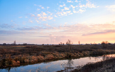Autumn landscape with a small river in a field at sunset