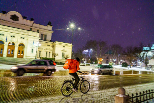 food currier running A snowy winter night in Sofia and the Bulgarian parliament building