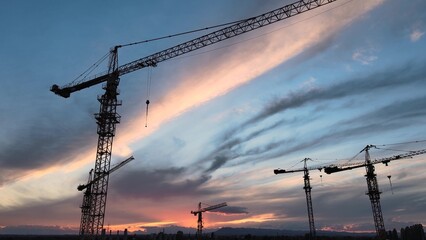 Silhouettes of Construction Cranes Under Colorful Sunset Sky. New Real Estate Development