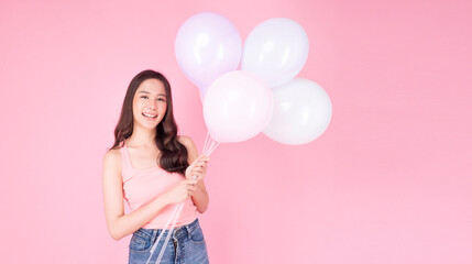Excited cheerful asian woman holding balloons and hands beside mouth smiling with toothy standing over isolated pink background. Joyful teenager girl with pastel balloons shocked  amazed expression.