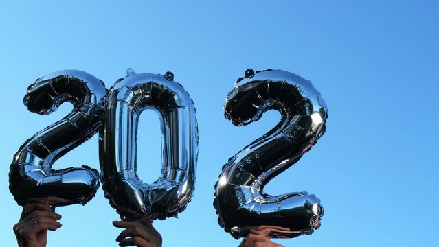 Silver foil number 2024 change to 2025 celebration new year balloon on blue sky background. Happy New year greetings concept. Hands holding balloons two thousand twenty-fourth change to two thousand