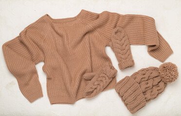 Sweater and winter hat with mittens on concrete background, top view.