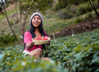 Mujer turista bastante joven con diadema tejida sosteniendo un tazón lleno de frutas y comiendo...