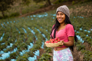 Mujer turista bastante joven con diadema tejida sosteniendo un tazón lleno de frutas y comiendo...