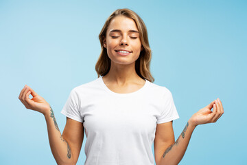 Portrait of attractive smiling woman with closed eyes wearing white t shirt meditating