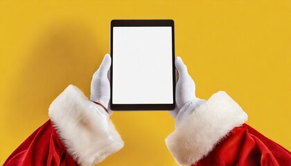 Image of hands of santa claus holding tablet with blank screen and copy space on yellow background	
