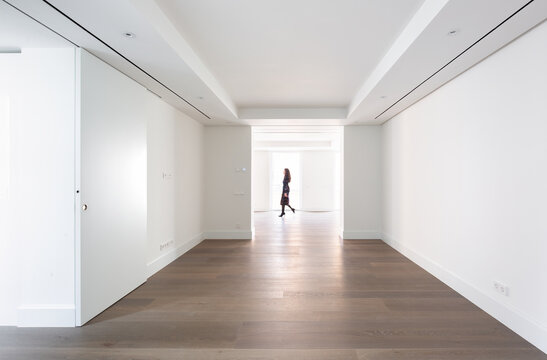 Minimalist hallway with hardwood floors and an unrecognizable woman walking through, surrounded by white walls and natural light