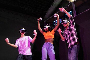 Exited multiracial friends jumping with victory while enjoying a virtual reality game, each wearing VR headsets and holding controllers, immersed in a digital adventure