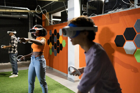 Side view of young multiracial friends engaged in virtual reality games wearing VR headsets and using handheld controllers in an indoor setting