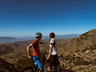 Two cyclists at the top of the mountain pointing at the route