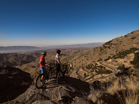 Two cyclists at the top of the mountain pointing at the route - Powered by Adobe