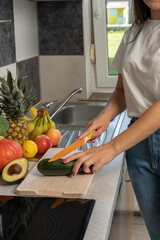 A young woman is cutting fruits and vegetables in the kitchen. There are fresh fruits and vegetables on the kitchen counter. The girl is cutting zucchini.