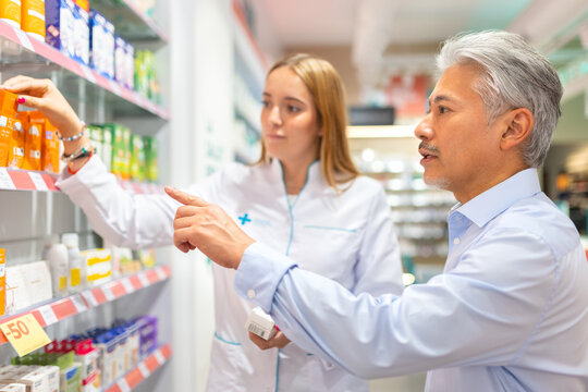 Female pharmacist and senior man choosing drug in shop